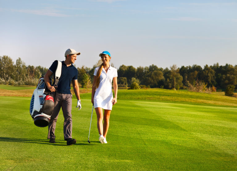 Young sportive couple playing golf on a golf course walking to the next hole